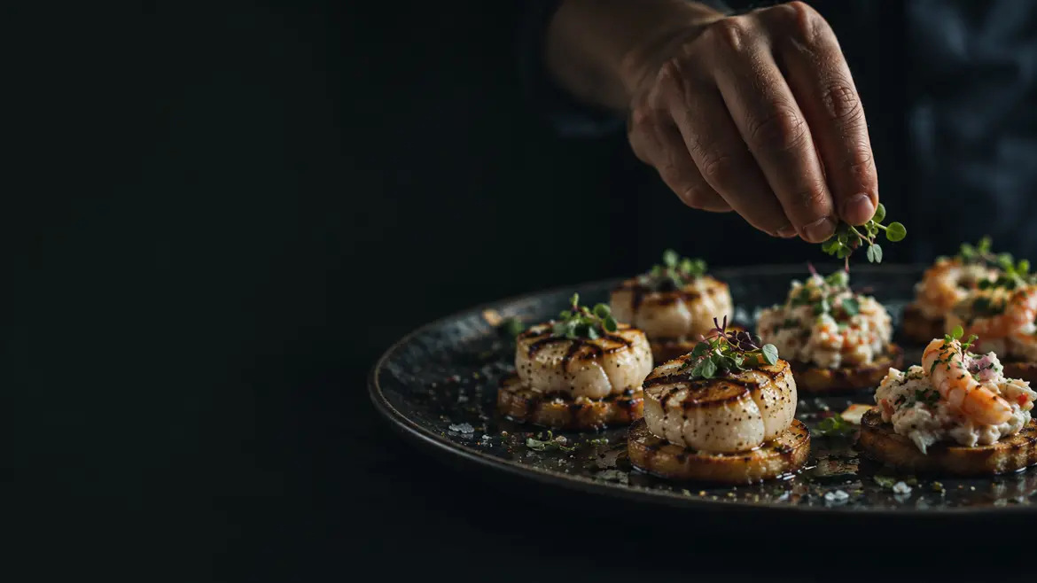 A hand garnishing scallop and prawn bites on a dark serving platter