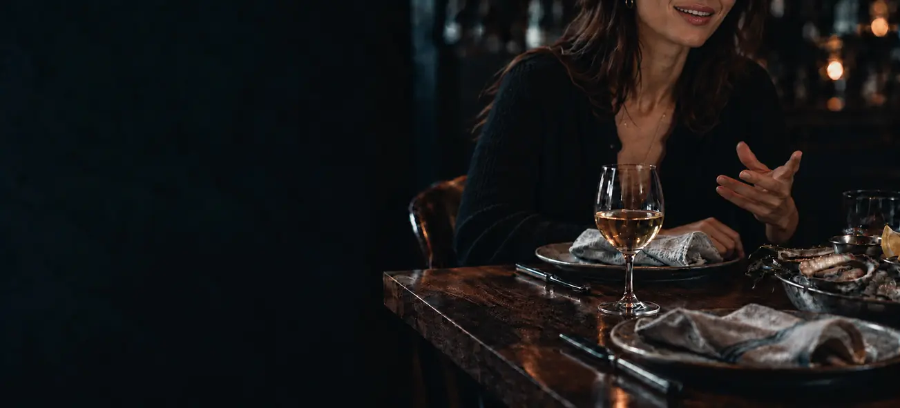 A guest enjoying conversation at a restaurant table set with wine and seafood