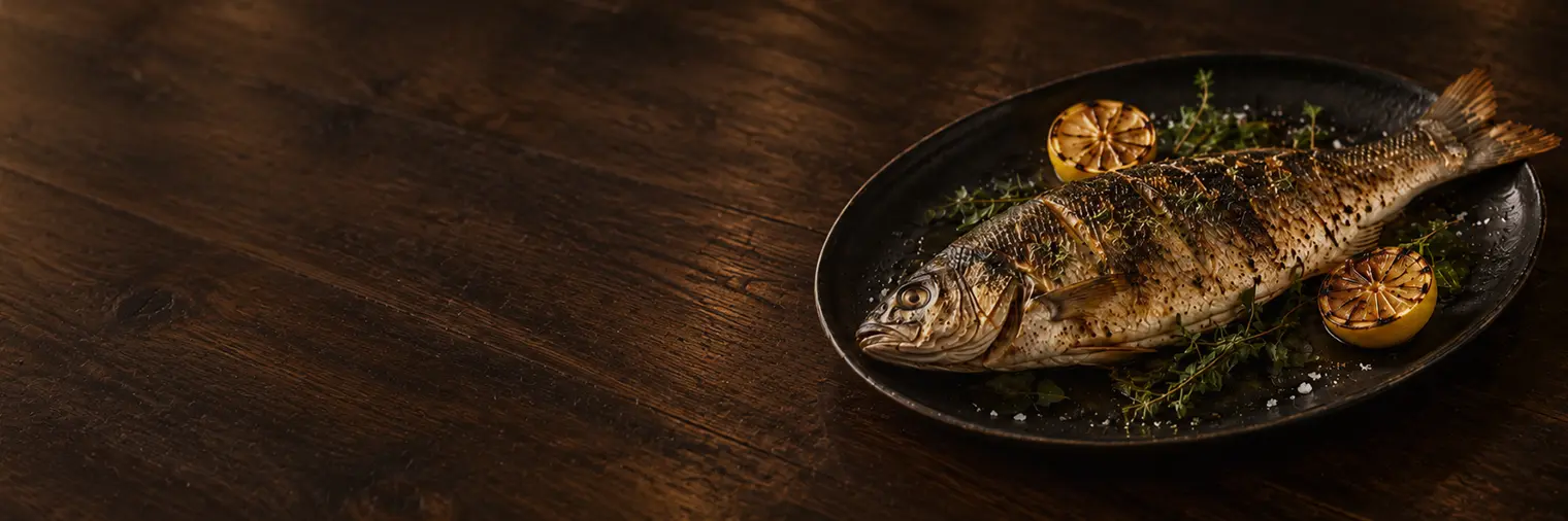 Whole grilled fish with charred lemon and herbs on a dark platter
