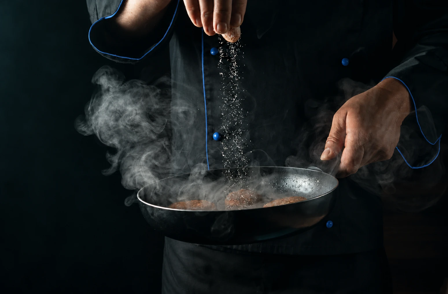 A chef seasoning food in a steaming pan