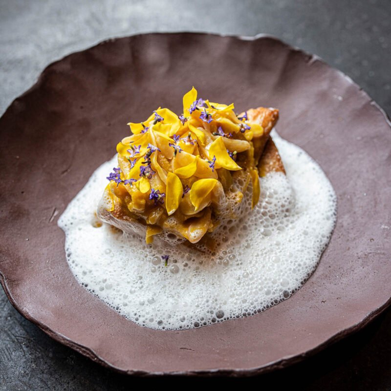 A plated dish with yellow petals, small purple flowers and a light foam
