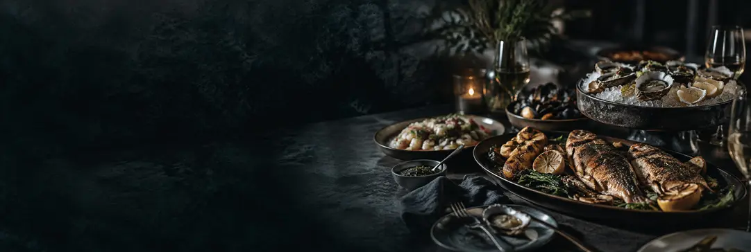 Seafood catering spread with grilled fish, oysters on ice, and shared plates on a dark table